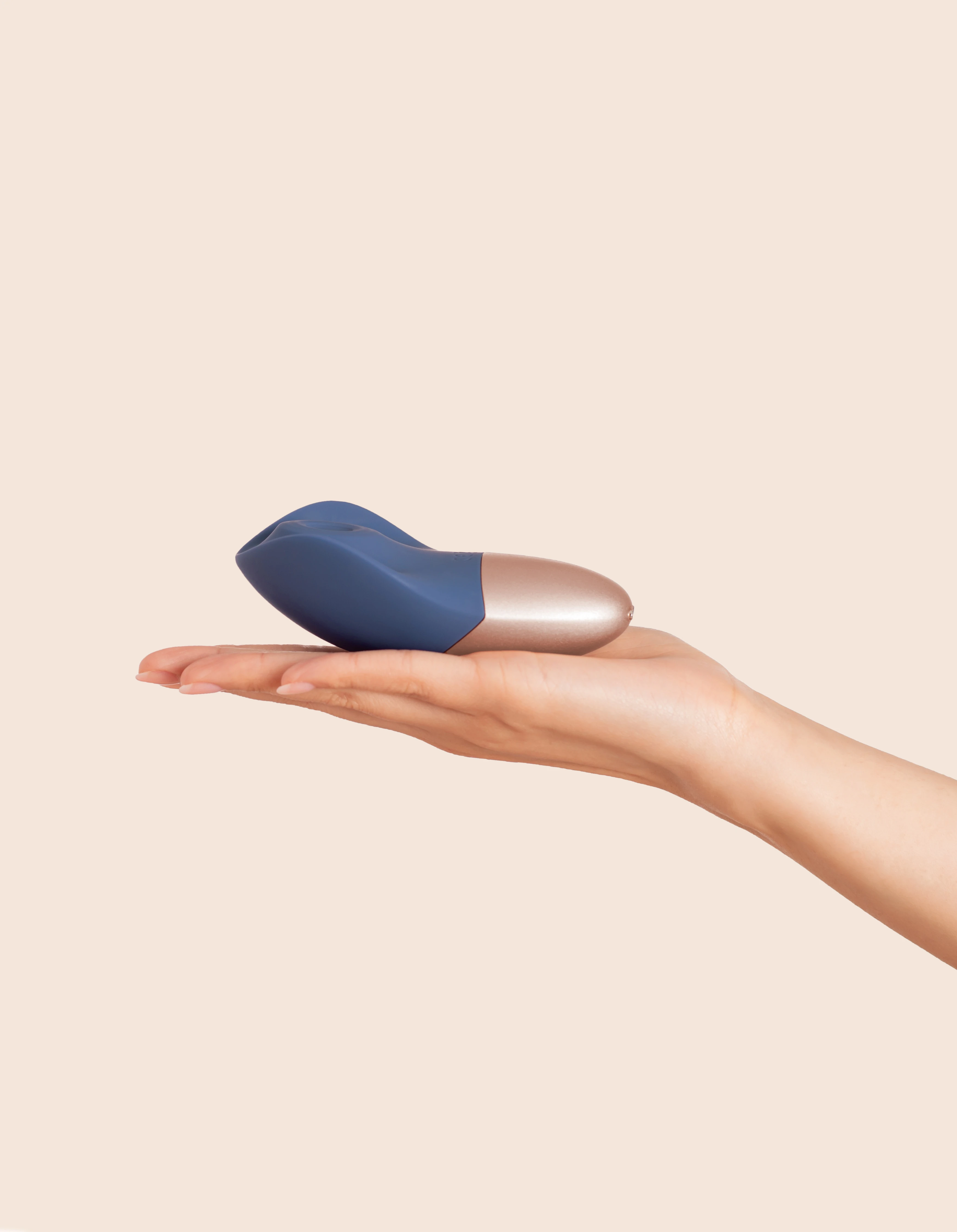 A blue and rose gold rechargeable silicone wand massager rests on a hand.