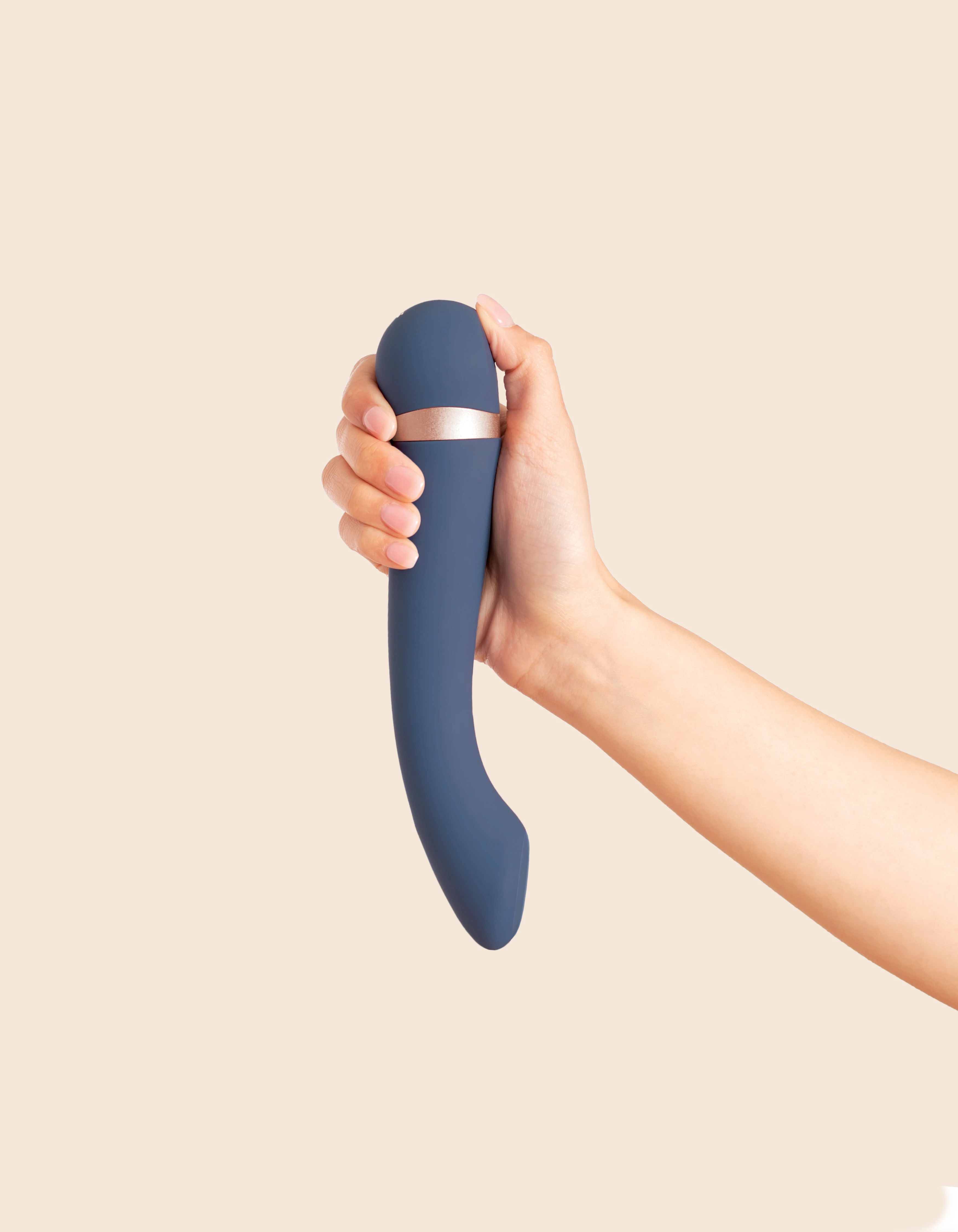 A hand holds a curved, dark blue vibrating massager with a rose gold band.