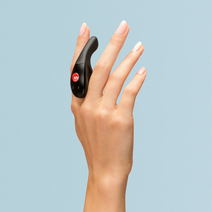 A black dual motor finger vibrator with red buttons is worn on a person's hand.