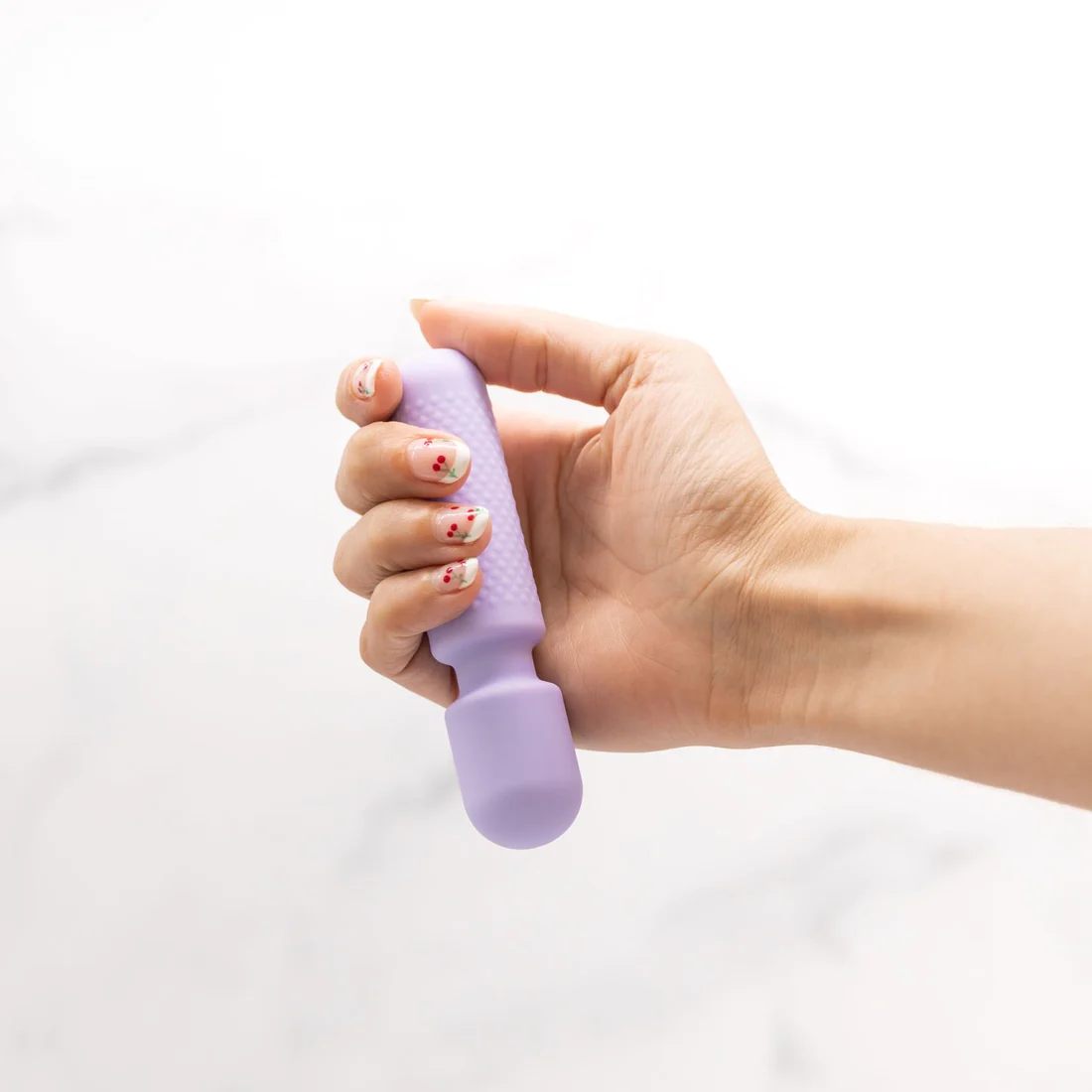 A hand holds a small, purple vibrator with a textured grip.