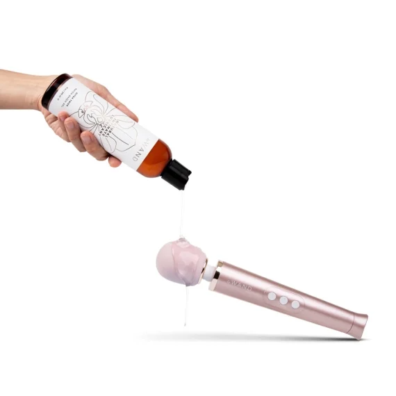A hand pours natural water-based lubricant from a bottle onto a pink vibrator.