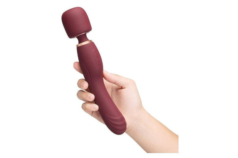 A maroon vibrating wand massager with a rounded head held in a hand.