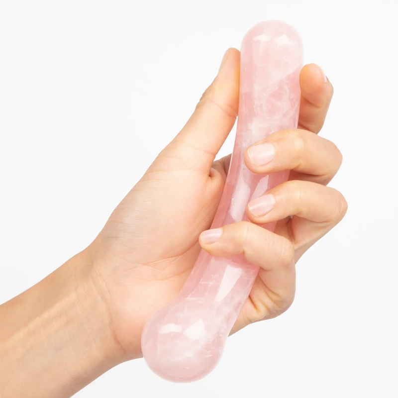 A hand holds a pink rose quartz crystal wand with a curved shape.