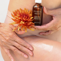 Foria Everyday Vulva Moisturizer with organic botanicals in a brown bottle held by hands with a flower.