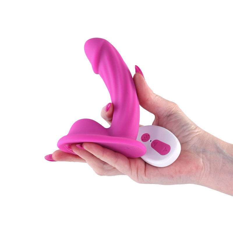 Curved pink vibrating dildo with a white wireless remote held in a hand.