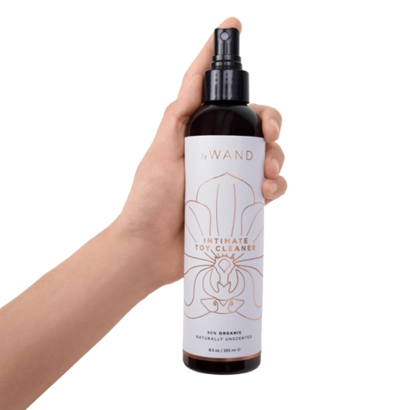 A hand holds a bottle of Le Wand Organic Intimate Toy Cleaner.