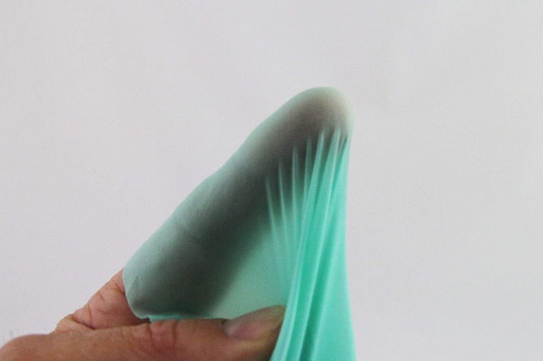 A hand holds a thin, teal-colored latex dental dam with vertical pleats.