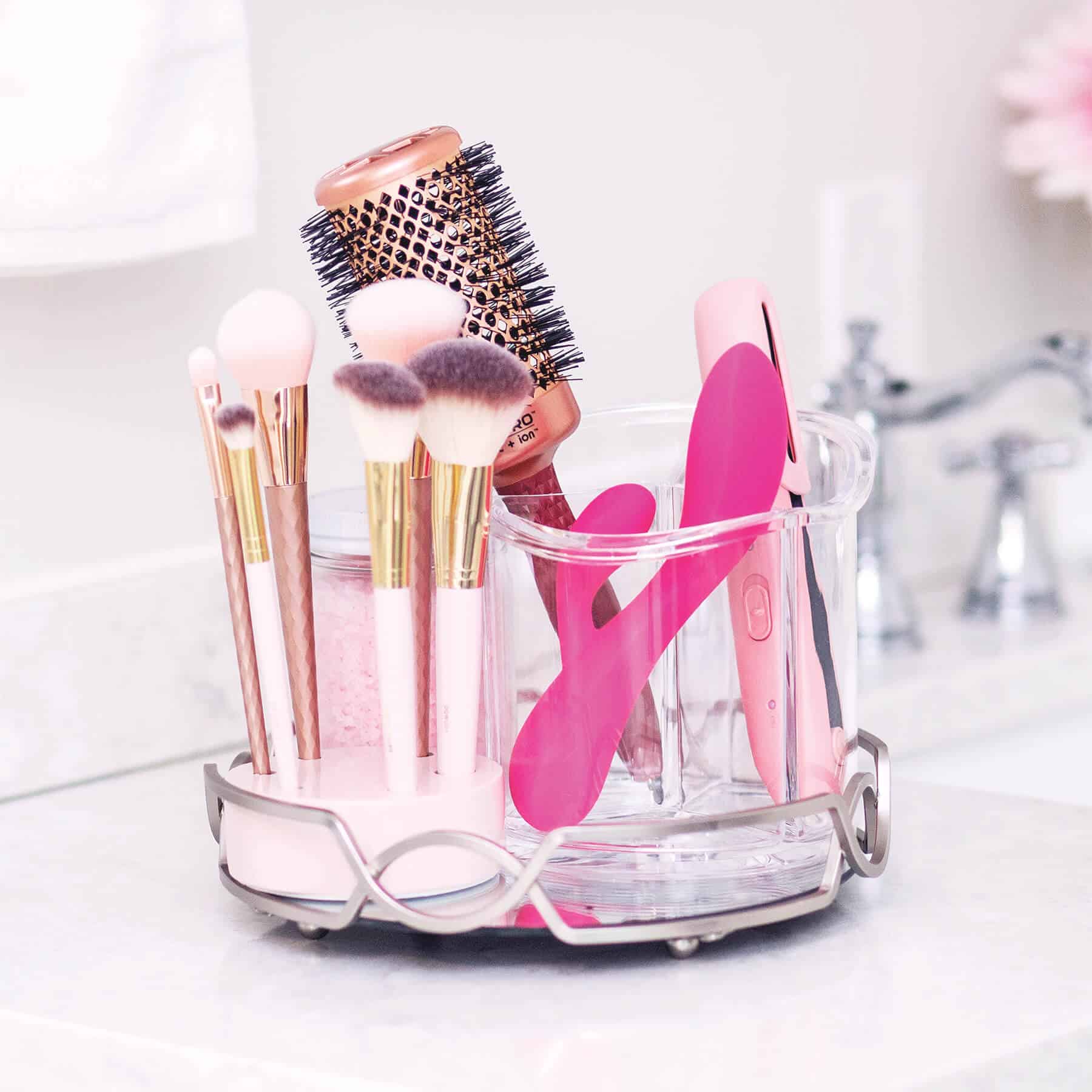Pink and rose gold makeup brushes and a pink hair styling tool in a clear organizer.
