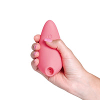 A pink clitoral arouser with a power button symbol is held in a hand.
