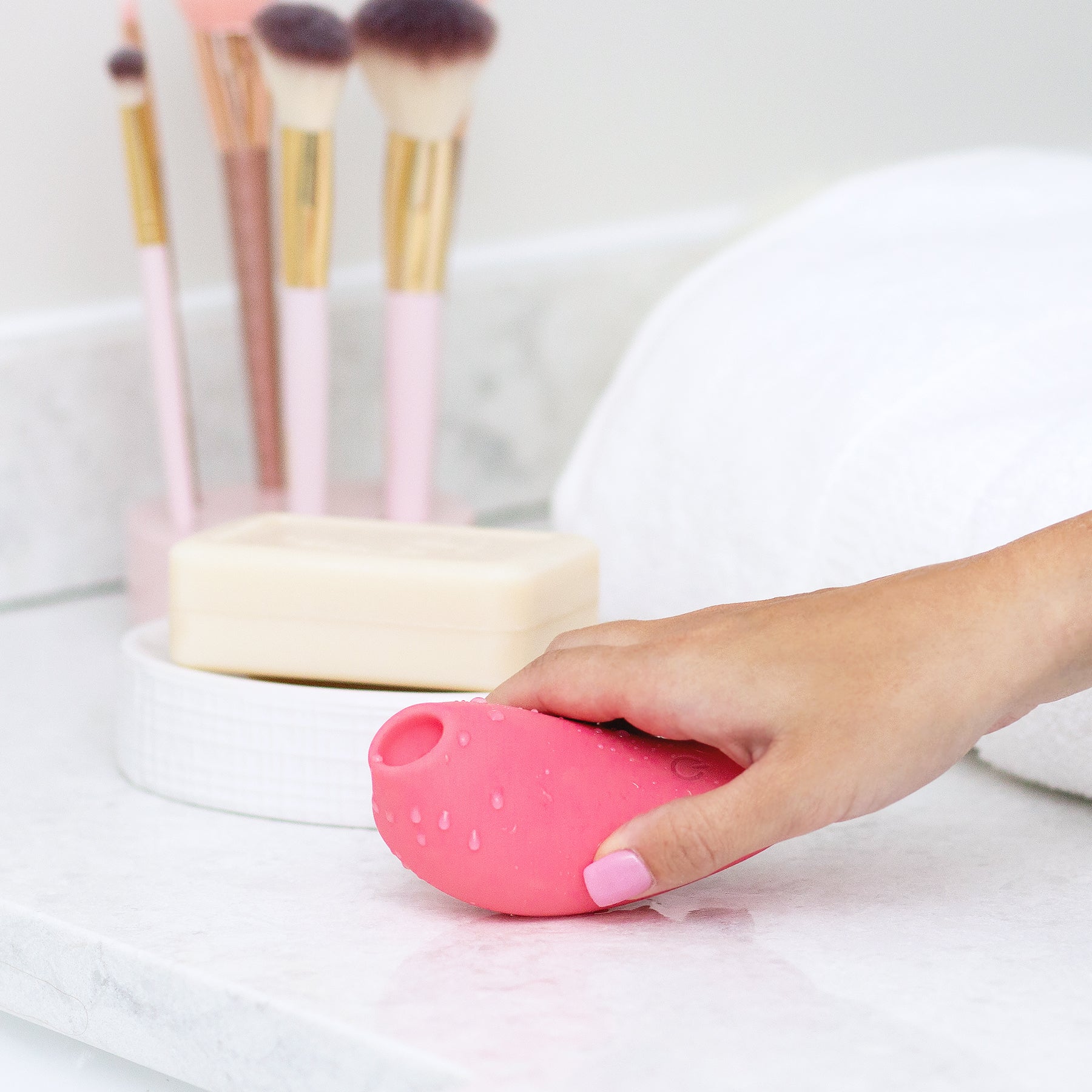 A hand holds a pink, water-covered clitoral massager with an opening.