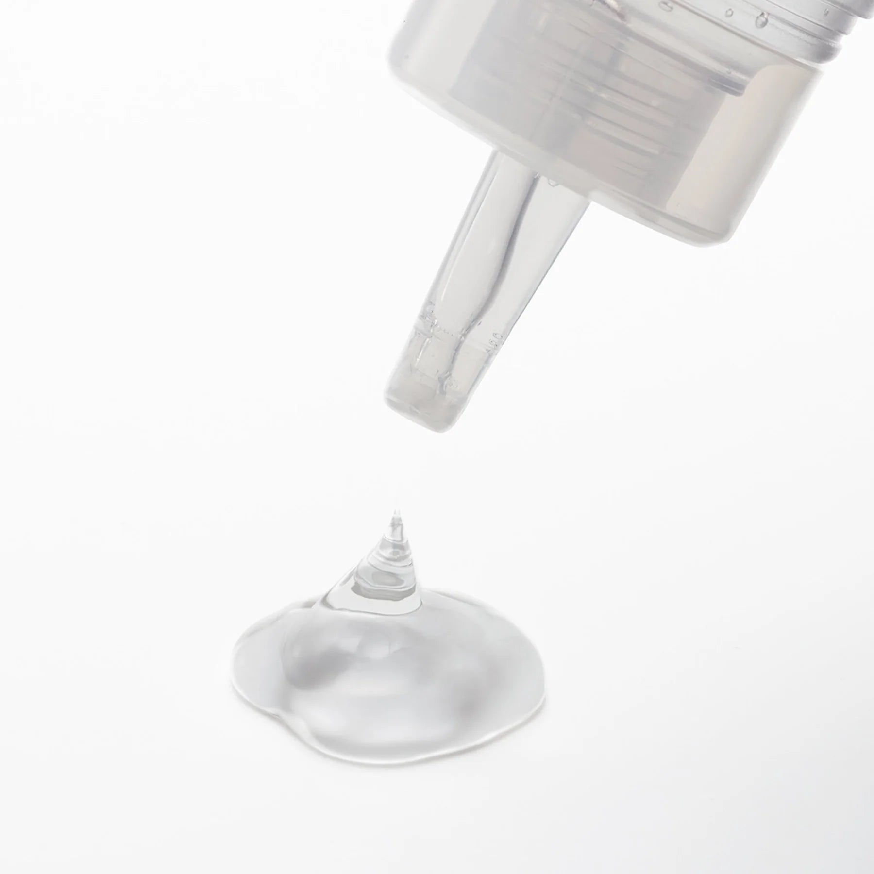 A clear, water-based lubricant is dispensed from a clear bottle onto a white surface.