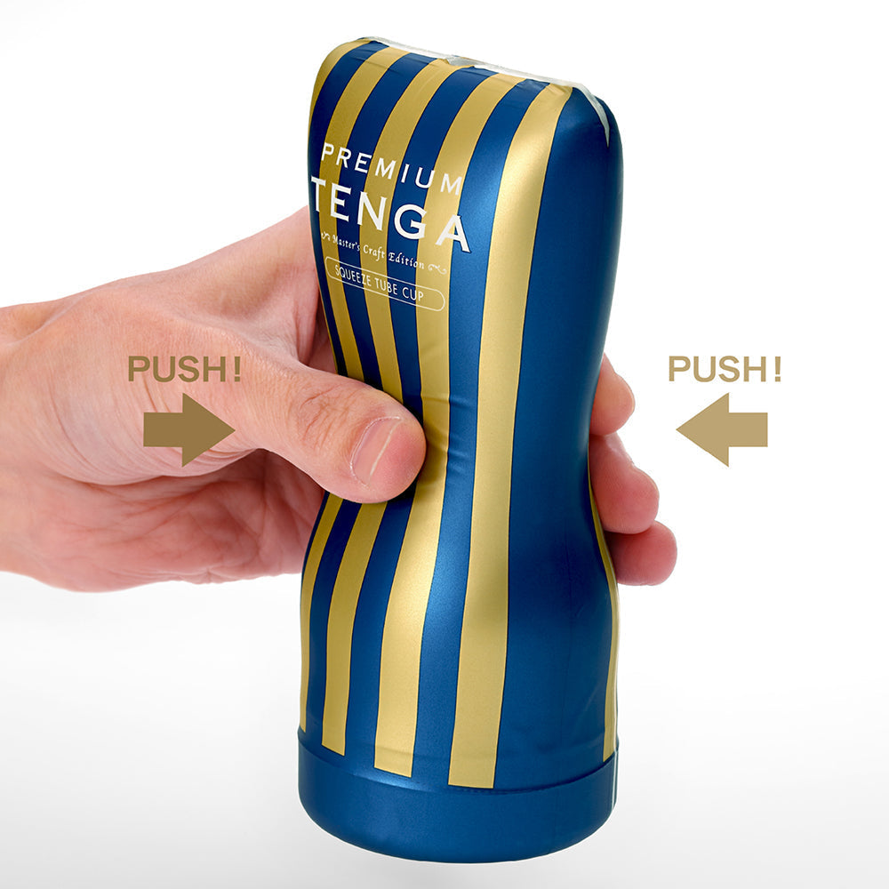 A hand squeezes a blue and gold striped Tenga masturbator.