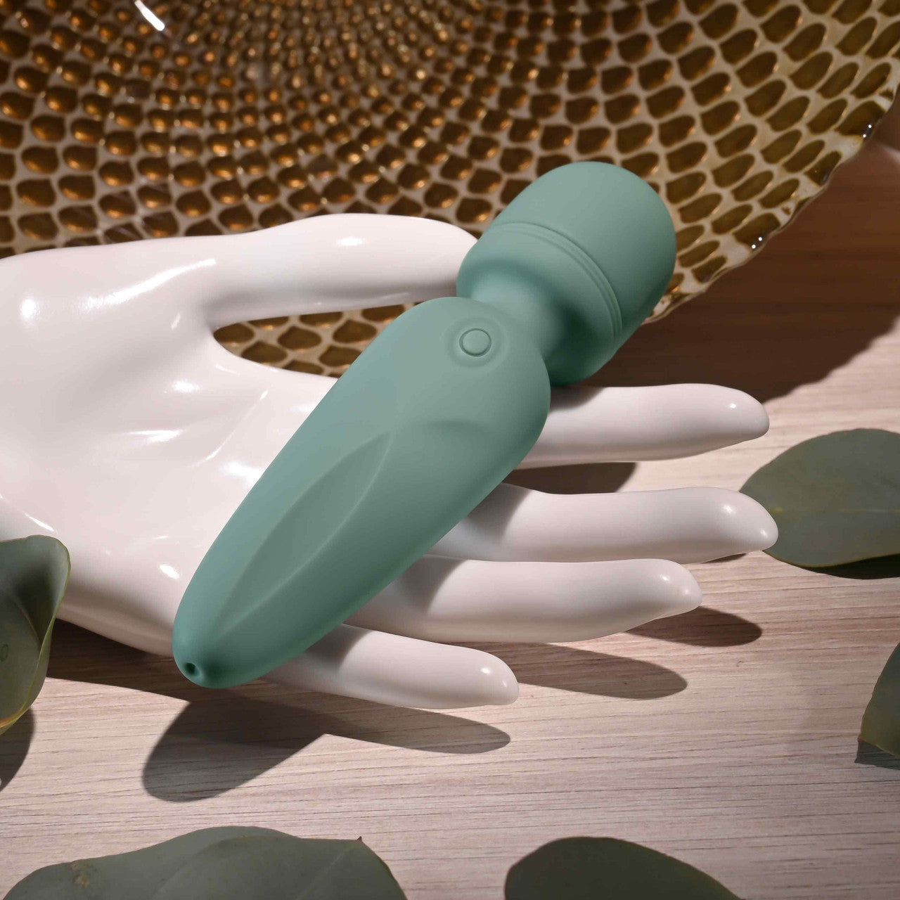 A teal silicone vibrator rests on a white hand-shaped display.