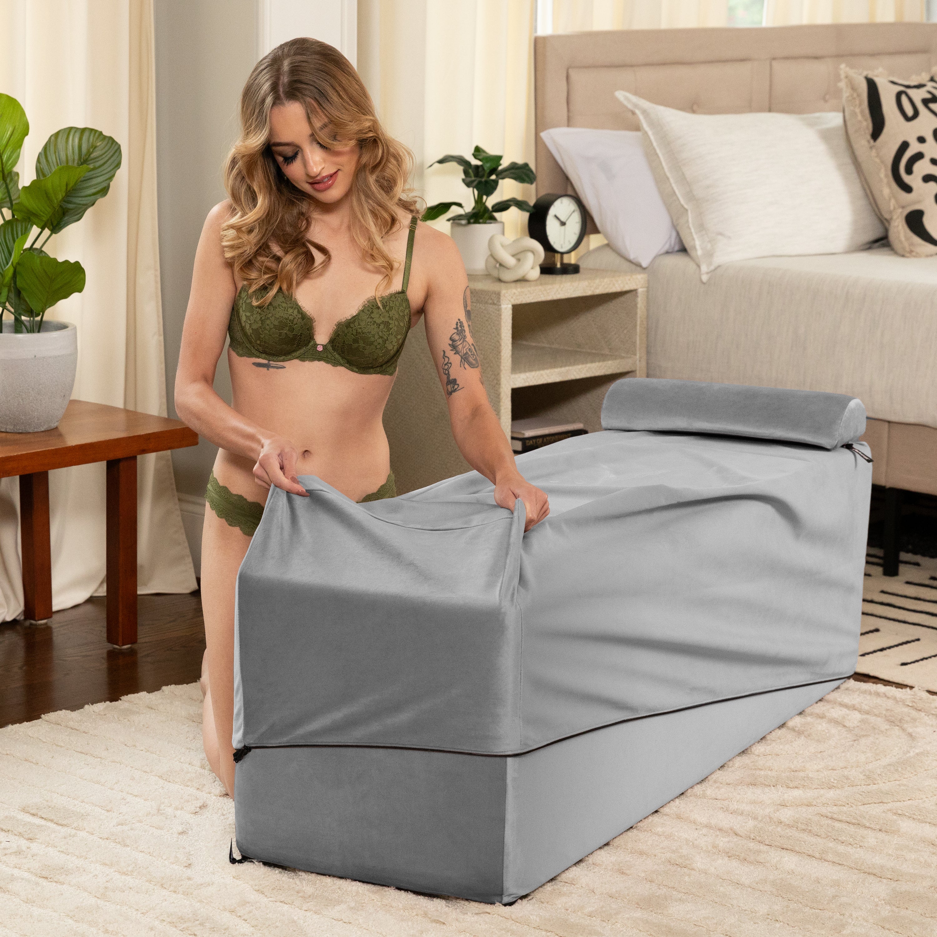 A woman in lingerie adjusts the grey velvet cover of a convertible sex chair and bed bench.