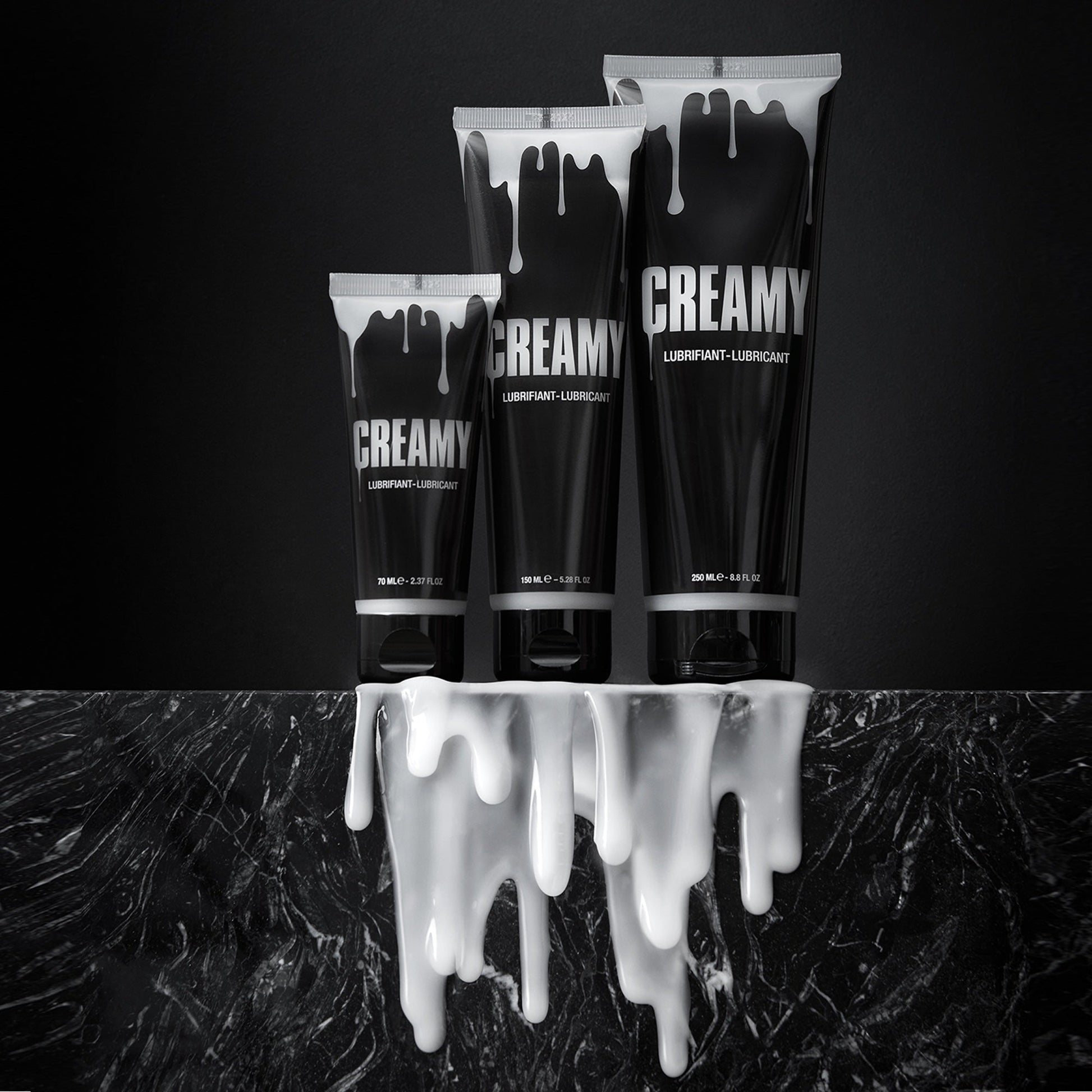 Three black tubes of Creamy lubricant with white drips on a dark marble surface.