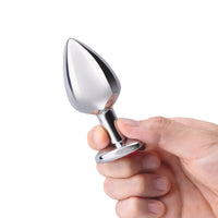 A hand holds a silver metal anal plug with a flared base.