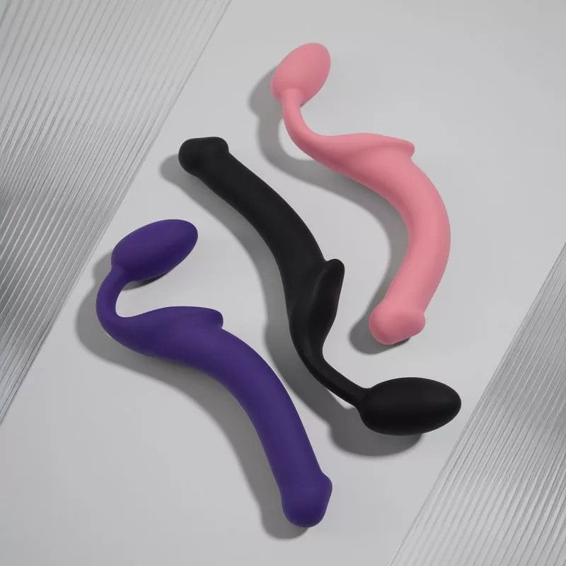 Three bendable silicone strap-ons in purple, black, and pink.