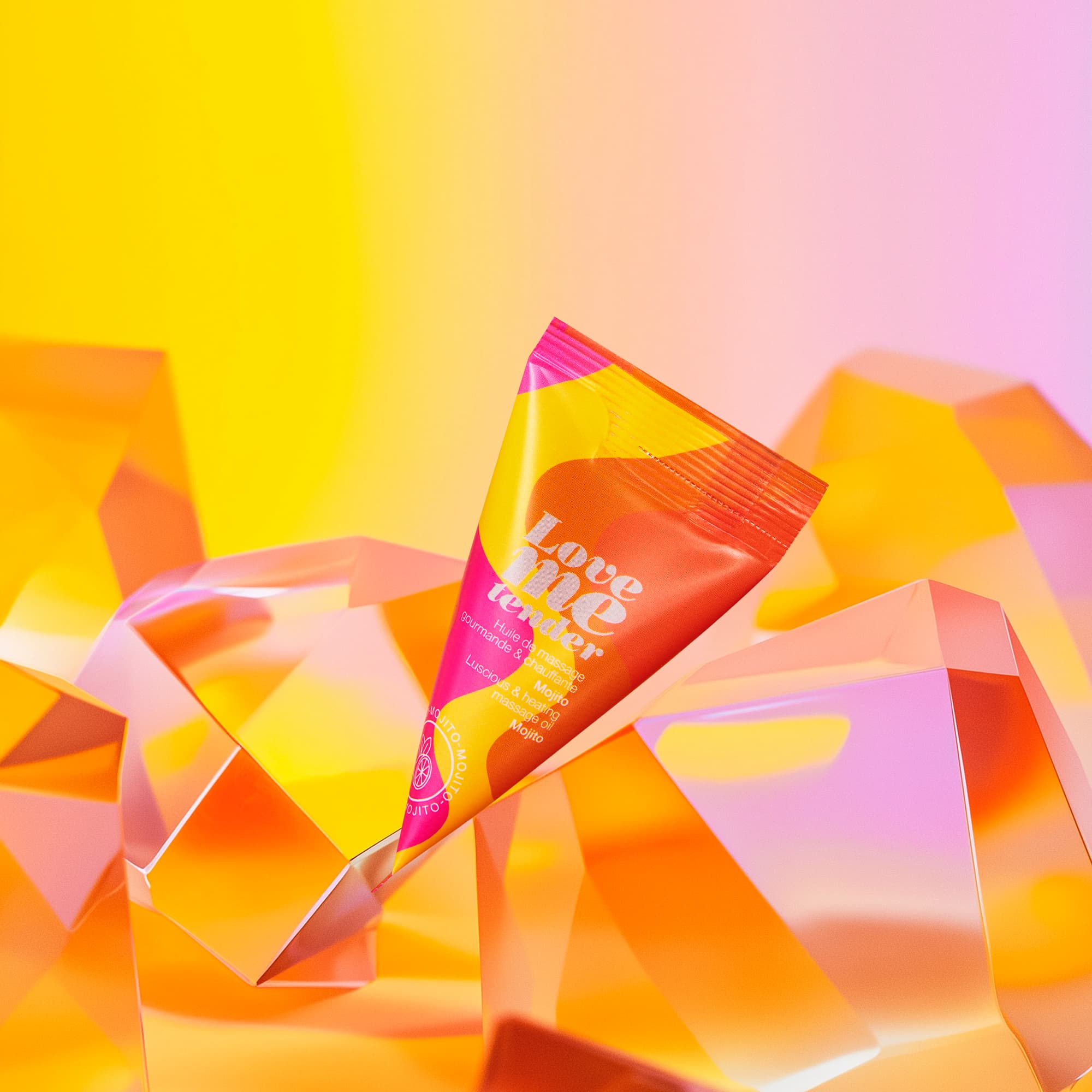 A tube of Love Me Tender Mojito warming massage oil rests on faceted orange and yellow crystals.