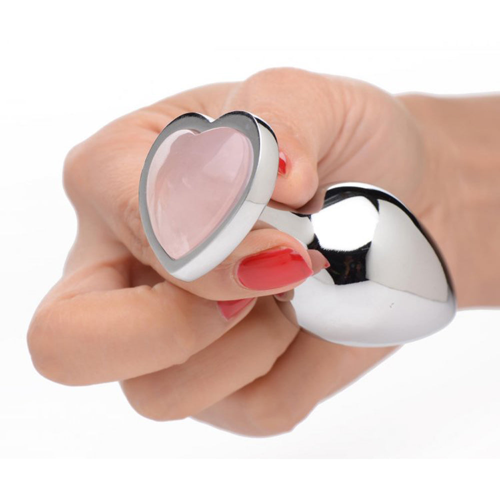 A hand holds a silver anal plug with a rose quartz heart gem.