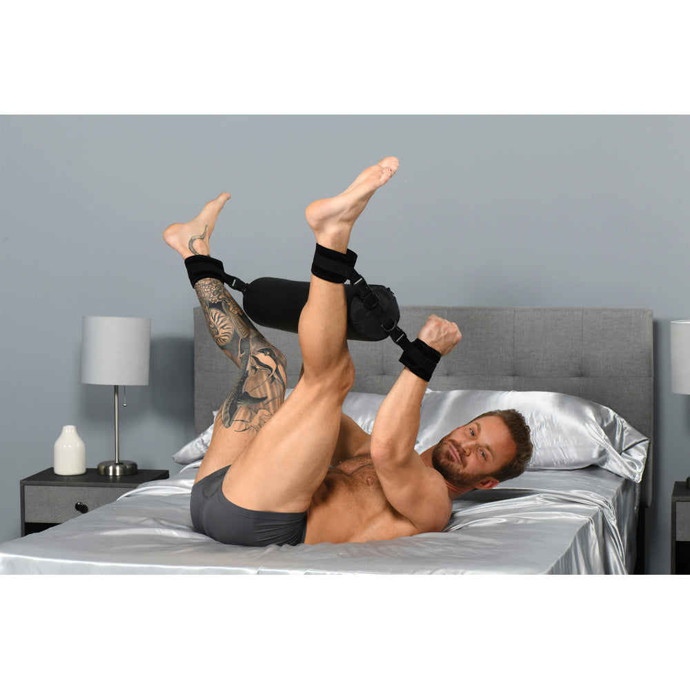 Man on bed with legs and wrists secured by a padded spreader bar restraint.