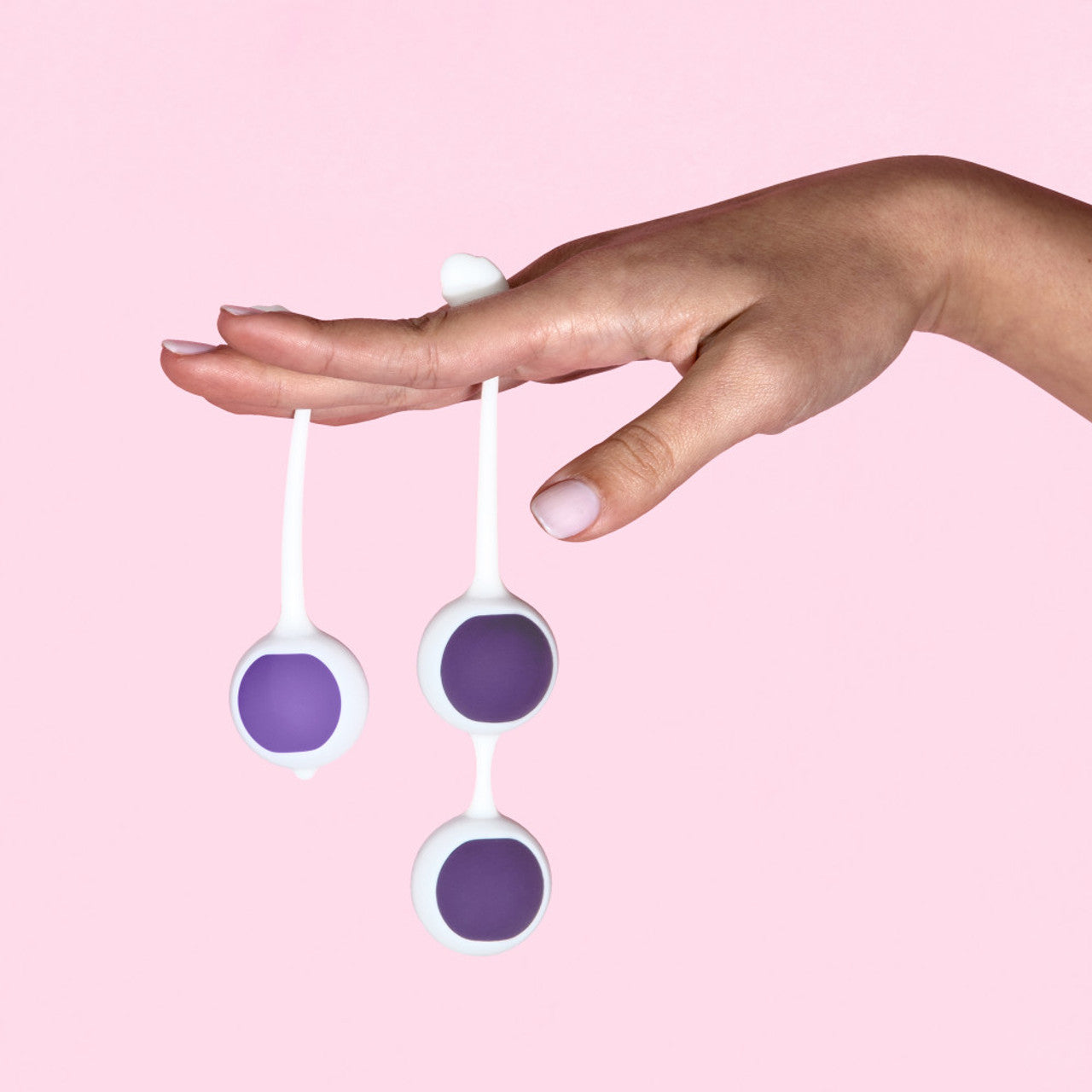 A hand holds three purple and white silicone balls on strings.