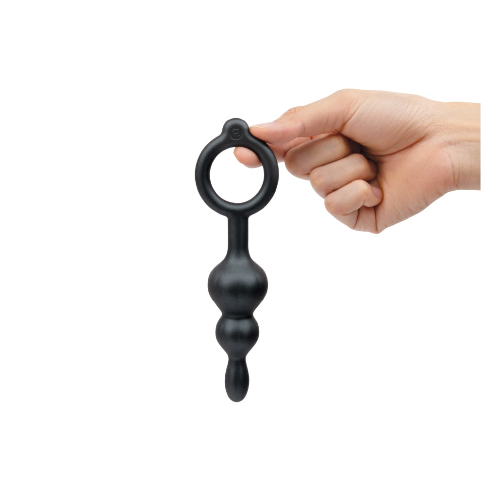 A hand holds a black silicone anal plug with a ring and three graduated beads.