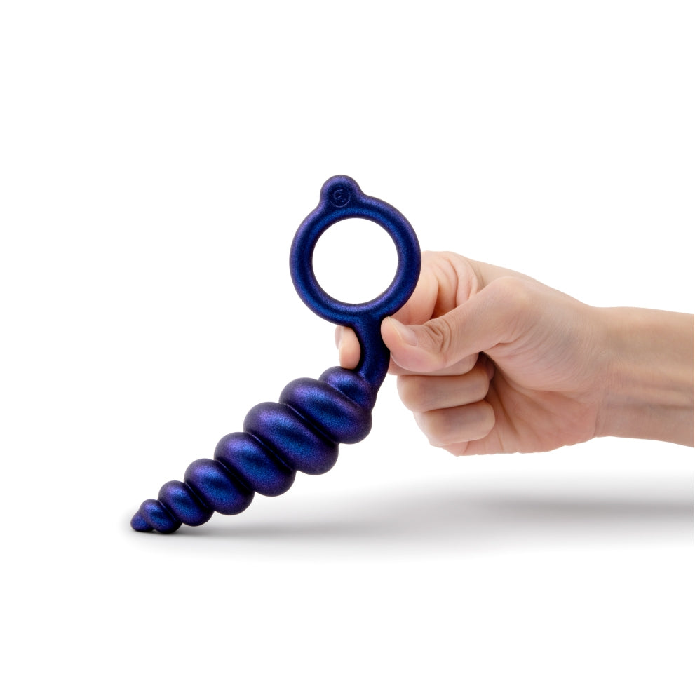 A hand holds a purple, ribbed anal plug with a ring handle.
