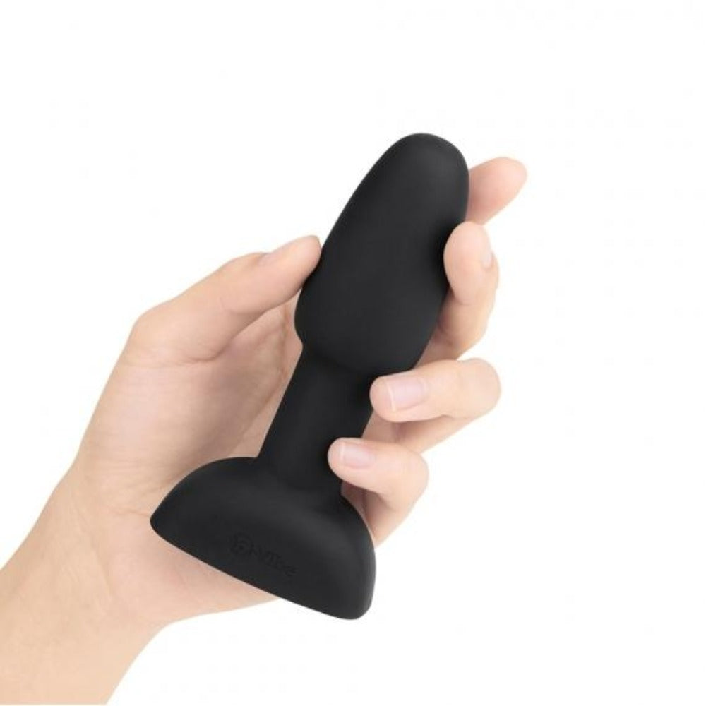 A hand holds a black vibrating rimming butt plug with a flared base.