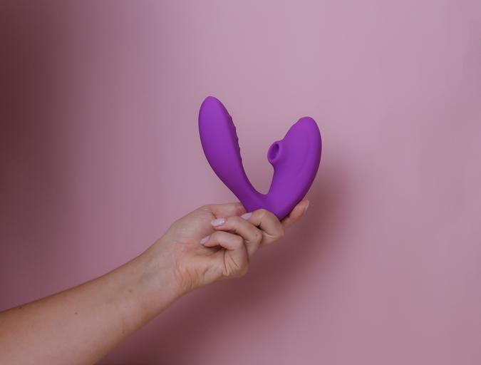 A purple suction and G-spot vibrator held in a hand.