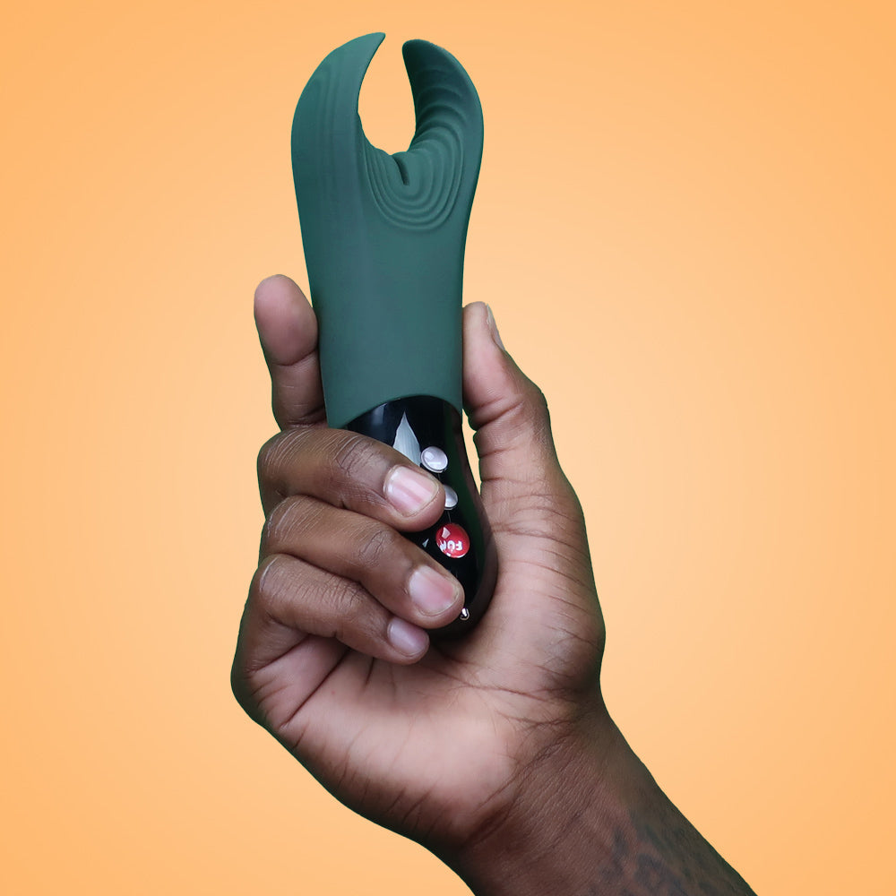 A hand holds a dark green vibrator with a black base and red button.