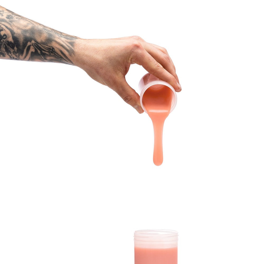 A hand pours light-toned silicone from a cup into a container.