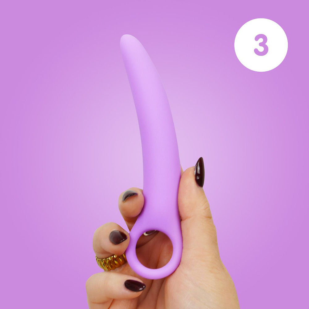 A hand holds a curved purple silicone dilator with a finger loop.