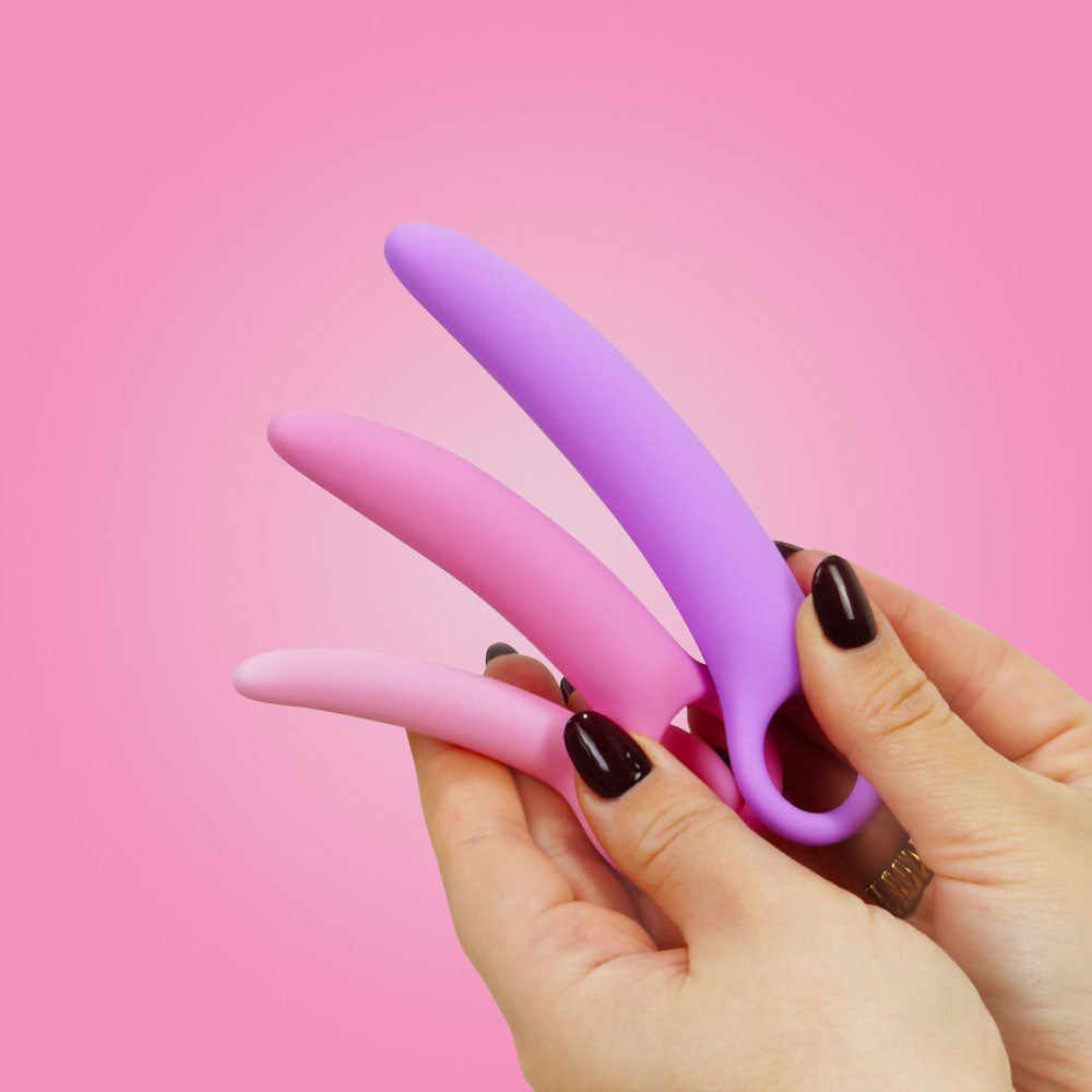Three curved silicone dilators in pink and purple held by hands.