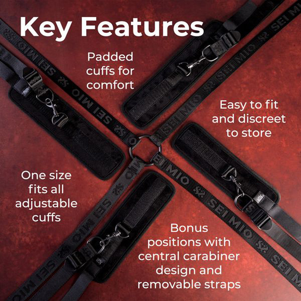 Adjustable bed restraint system with padded cuffs and central carabiner.