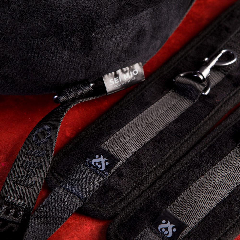 Black padded restraint system with adjustable straps and metal clips.