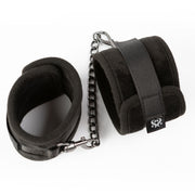 Padded black ankle restraints with adjustable velcro and a metal chain.