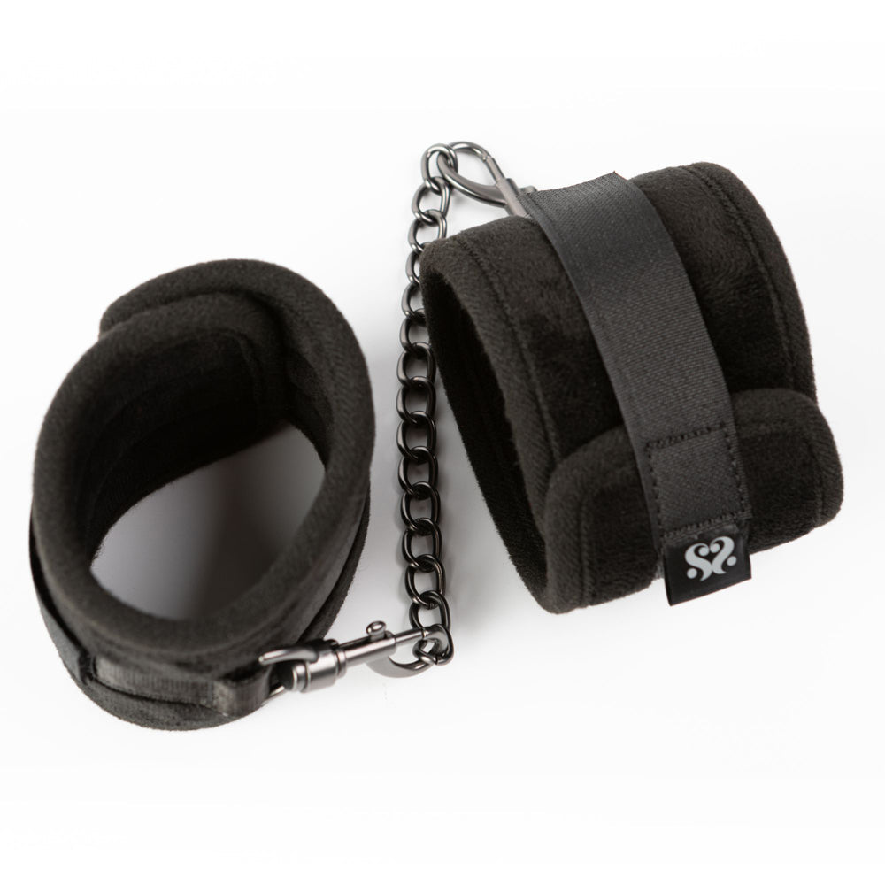 Padded black ankle restraints with adjustable velcro and a metal chain.