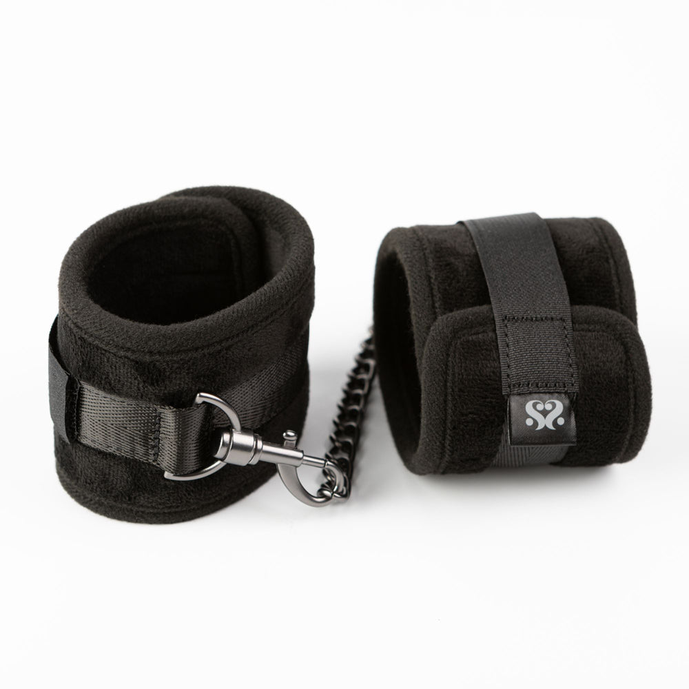 Black padded ankle restraints with adjustable velcro and a metal chain.