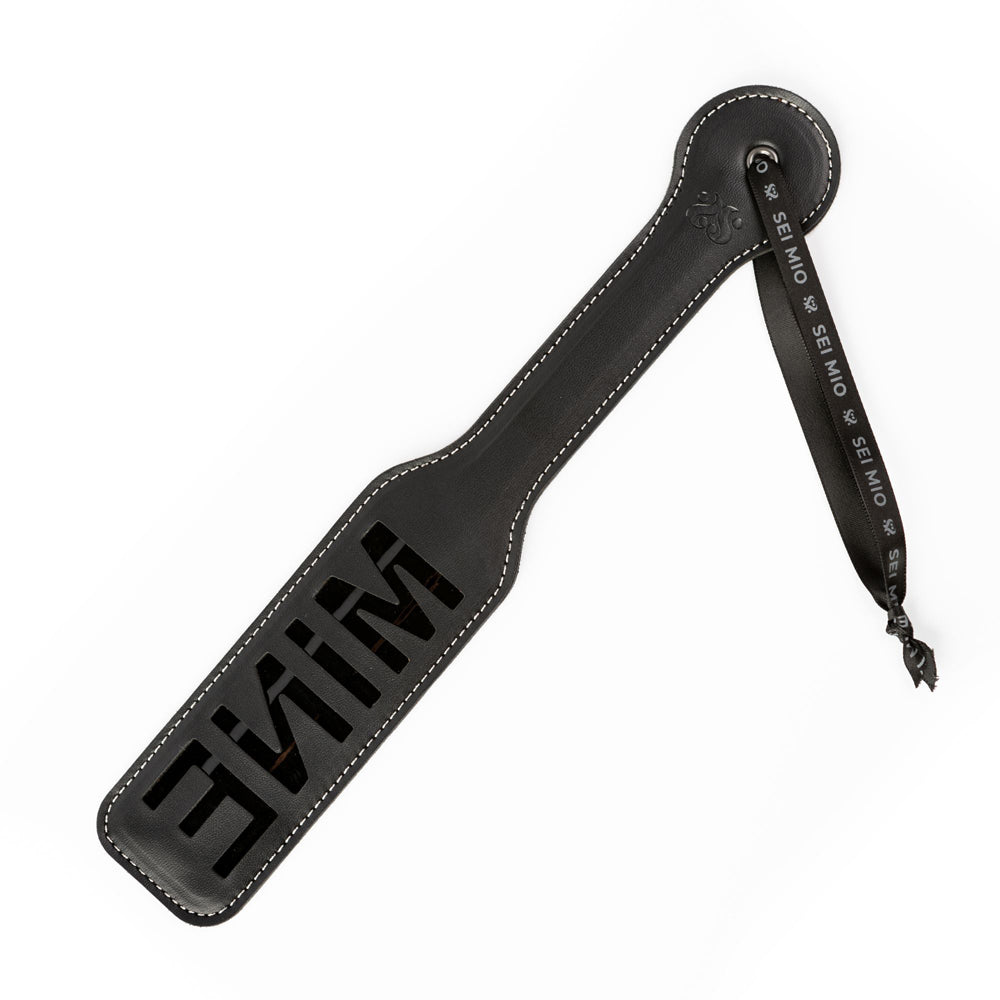 Black faux leather spanking paddle with "MINE" cut out and a wrist strap.