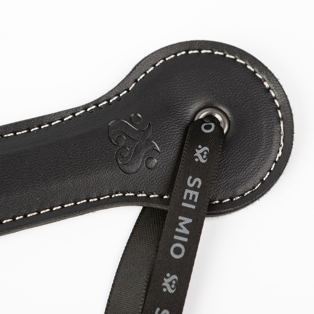 Black faux leather spanking paddle with white stitching and a "Sei Mio" ribbon.