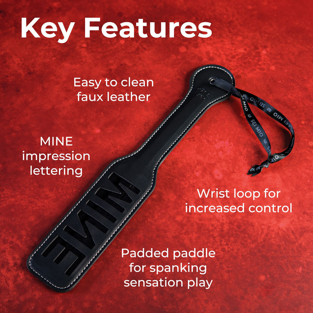 Black faux leather spanking paddle with "MINE" cut-out and wrist loop.