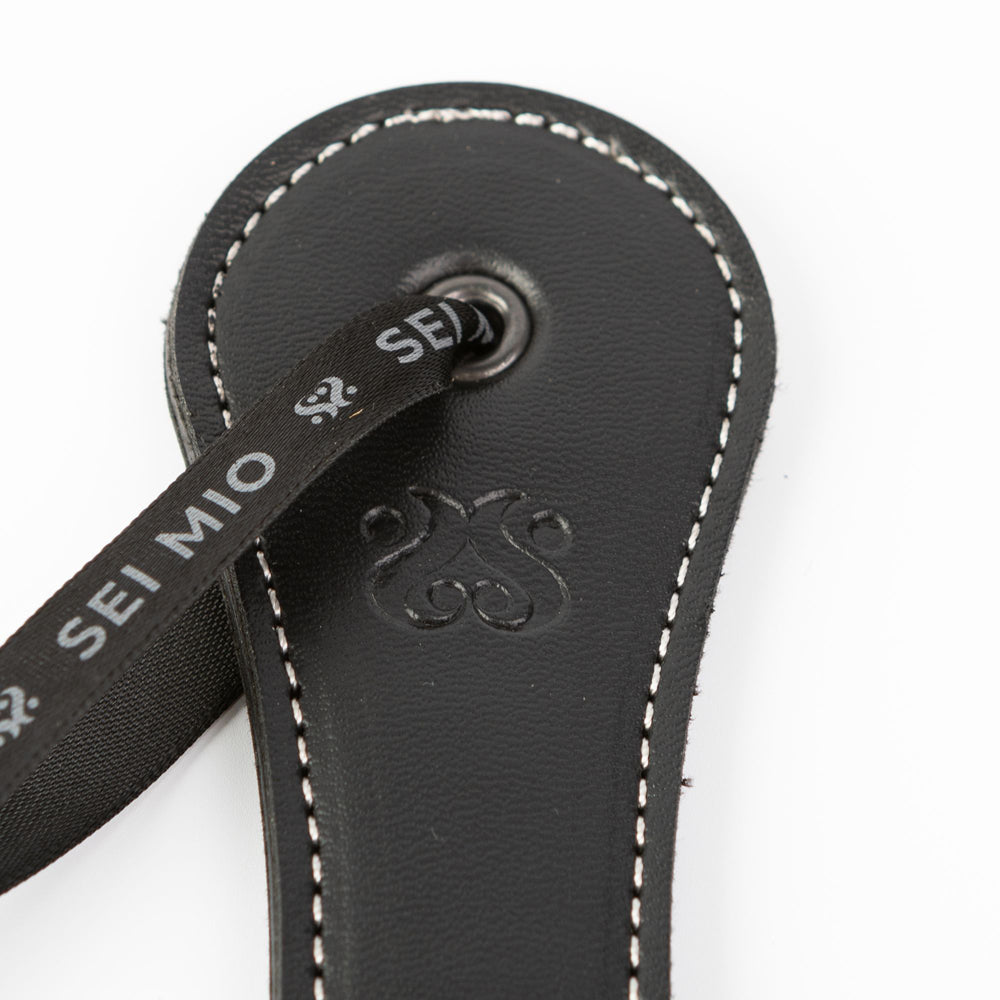 Black faux leather spanking paddle with "Sei Mio" ribbon and embossed logo.