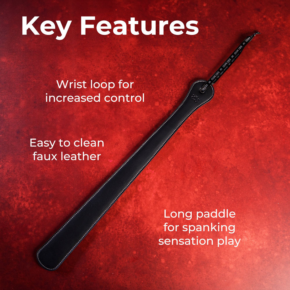 Black faux leather spanking paddle with wrist loop and white stitching.