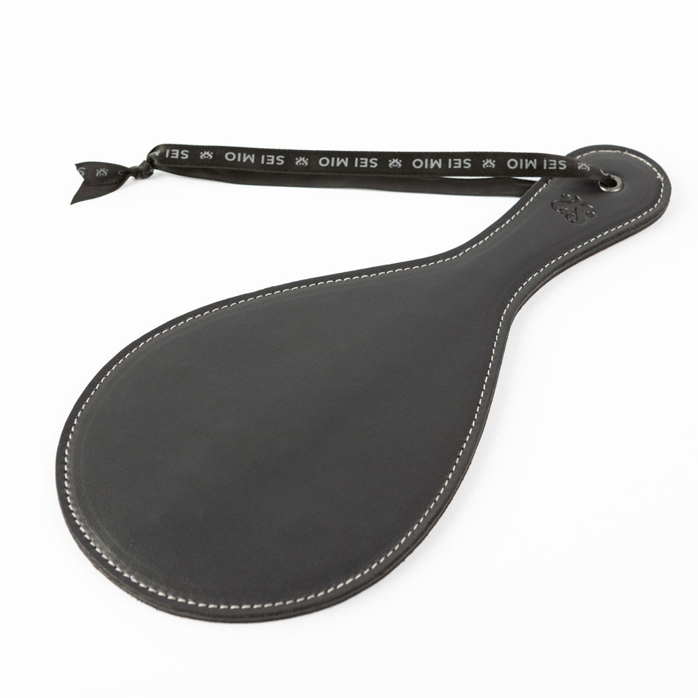 Black faux leather round spanking paddle with white stitching and a branded ribbon.