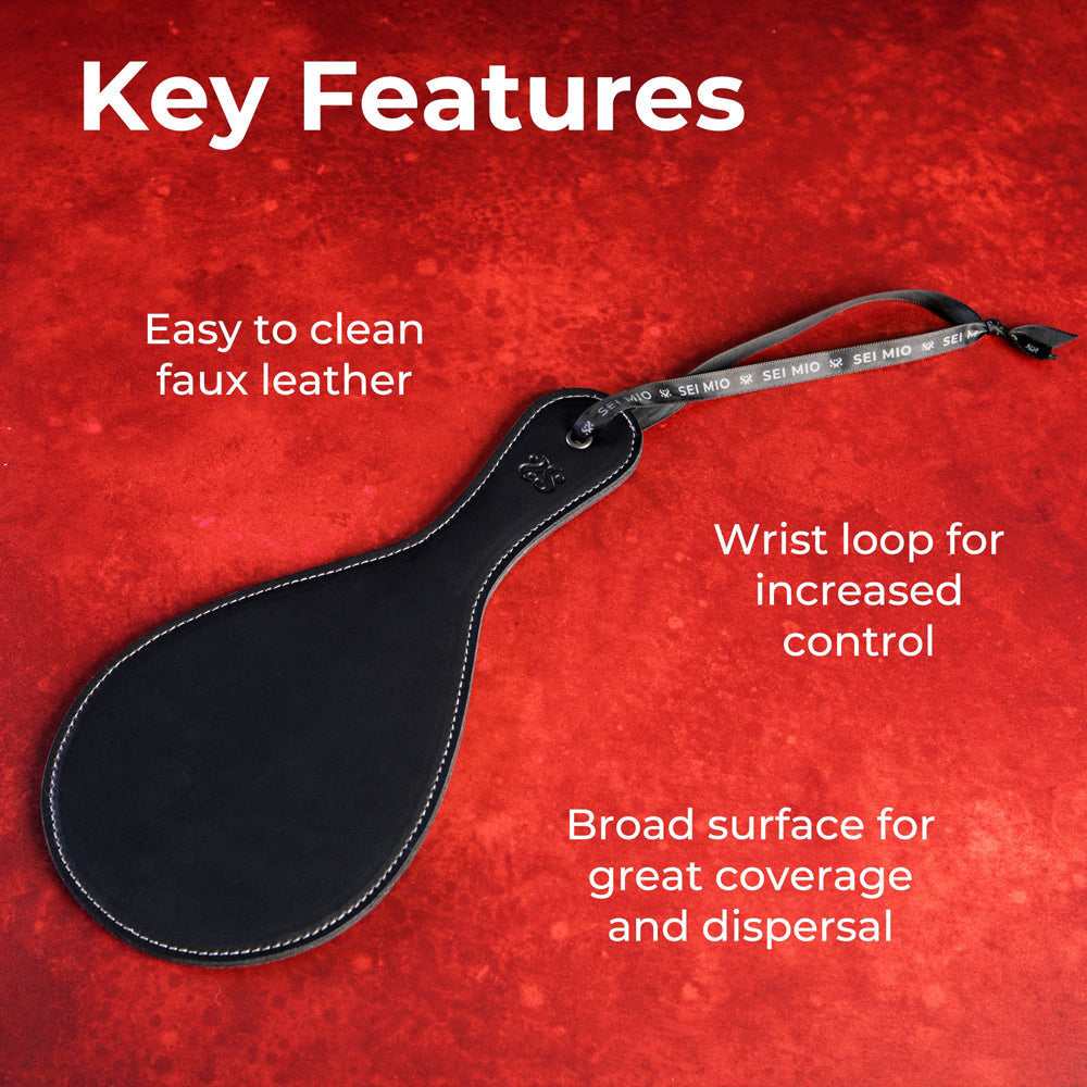A black faux leather round spanking paddle with a wrist loop.