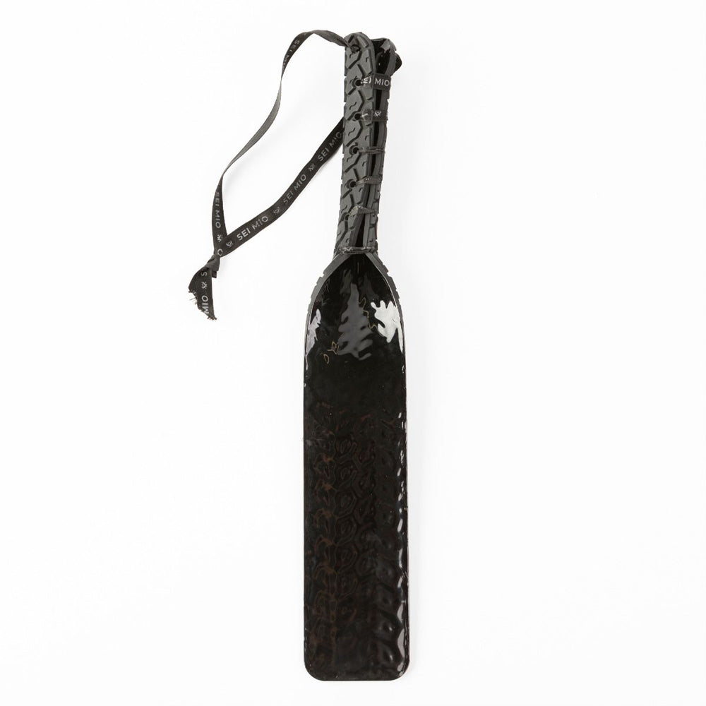 Black silicone spanking paddle with tire tread texture and a ribbon.