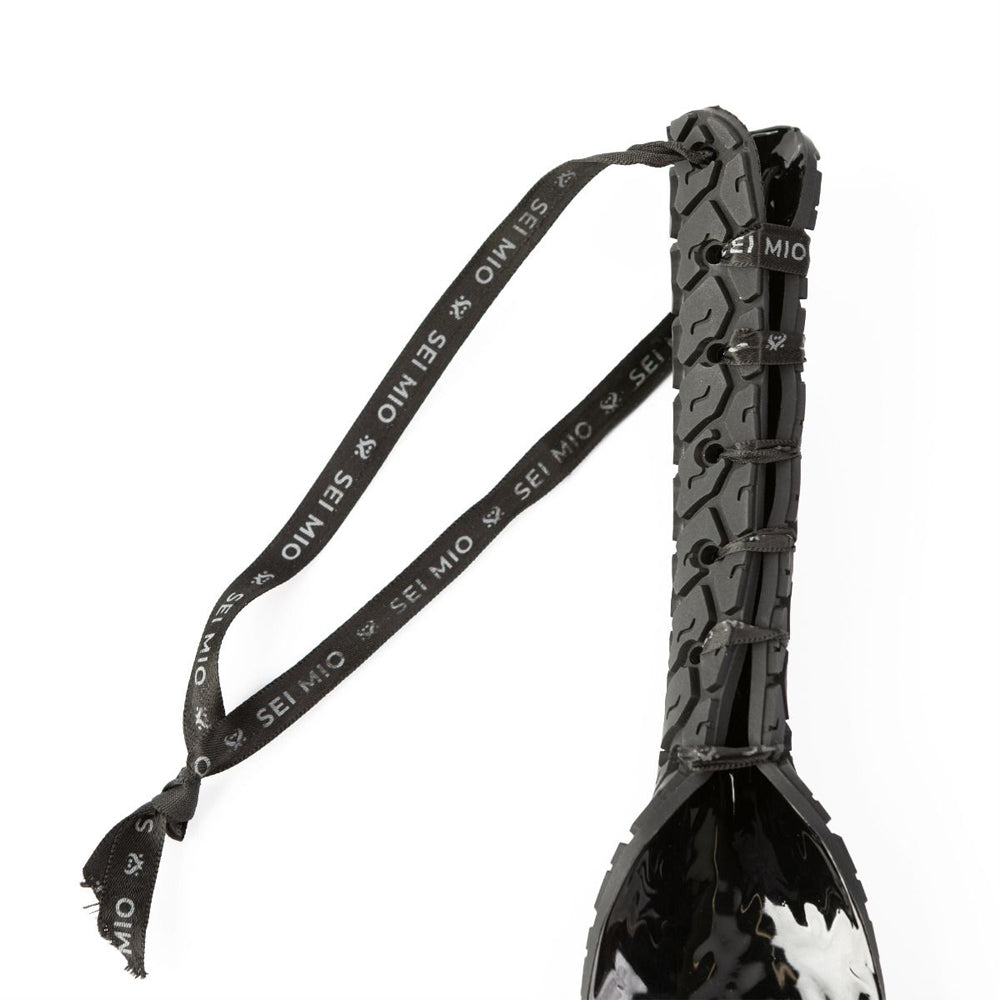 Black silicone spanking paddle with tire tread texture and a branded ribbon.