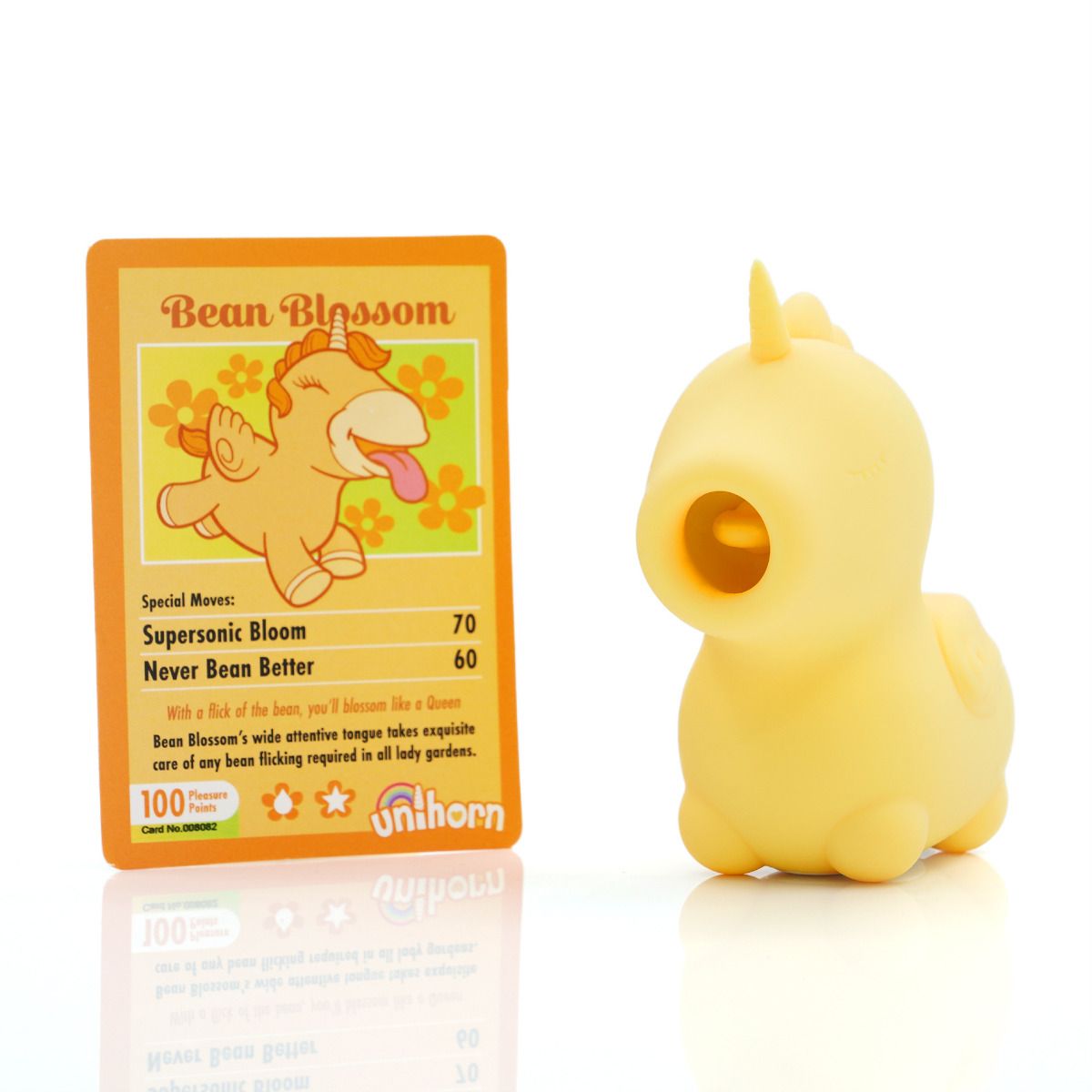 A yellow unicorn-shaped silicone tongue vibrator next to a trading card.