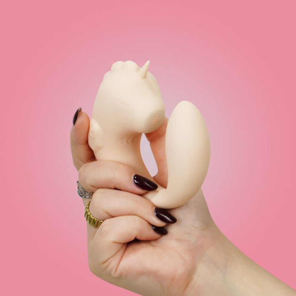 A hand holds a beige unicorn-shaped silicone massager with a curved tail.