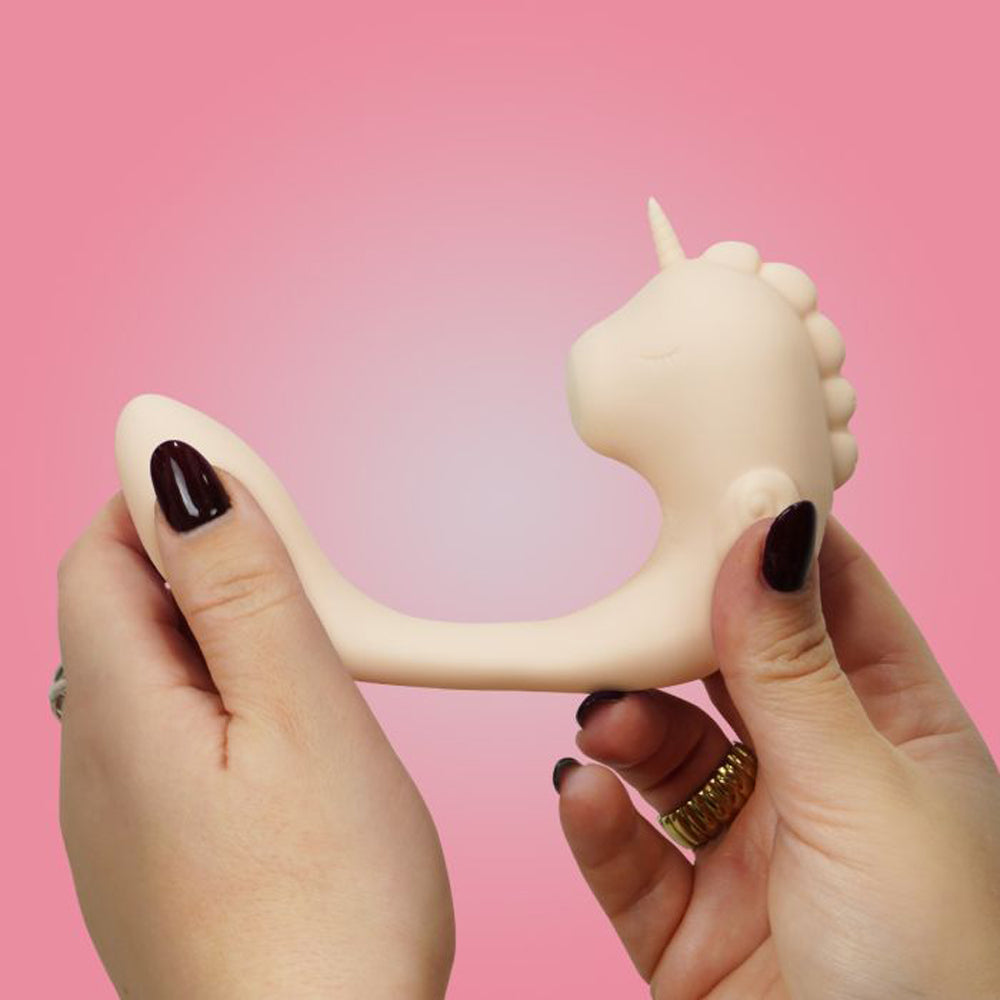 A beige unicorn-shaped silicone massager held by two hands.